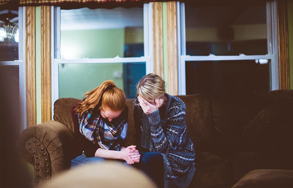 Mother and daughter sitting on sofa in a room, looking worried