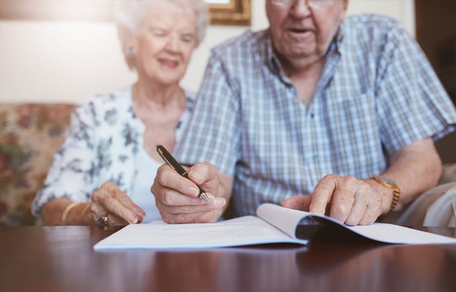 Elderly Caucasian man and woman sitting at home and signing some paperwork.